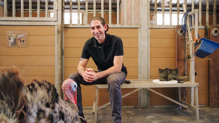 Student sits in a barn near a turkey