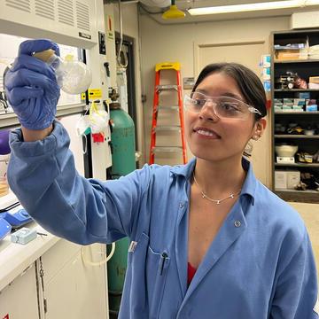 student in lab coat holds examines equipment