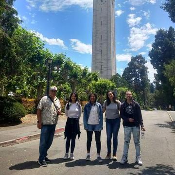 Five individuals stand on a path in front of a bell tower.